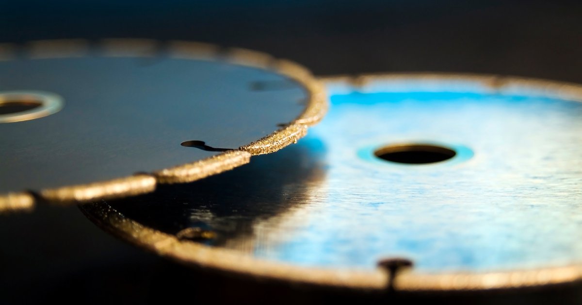 Two diamond saw cutting blades, one black and one chrome, are overlapping one another. The background is blurred.