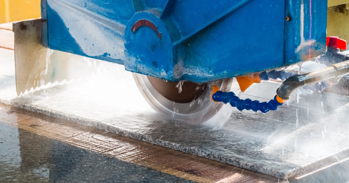 A close-up of a large bridge saw machine with diamond blades cutting into a slab of granite while spraying water.