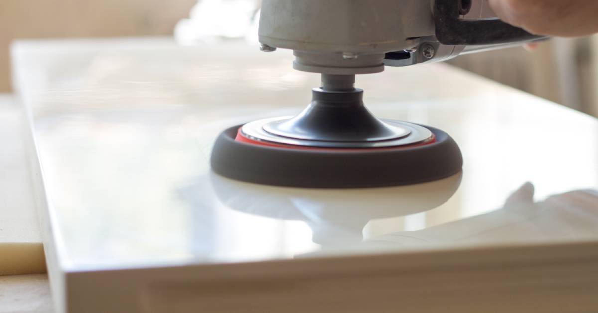 A close-up of a person holding a stone polisher with a black pad and polishing a white marble countertop.