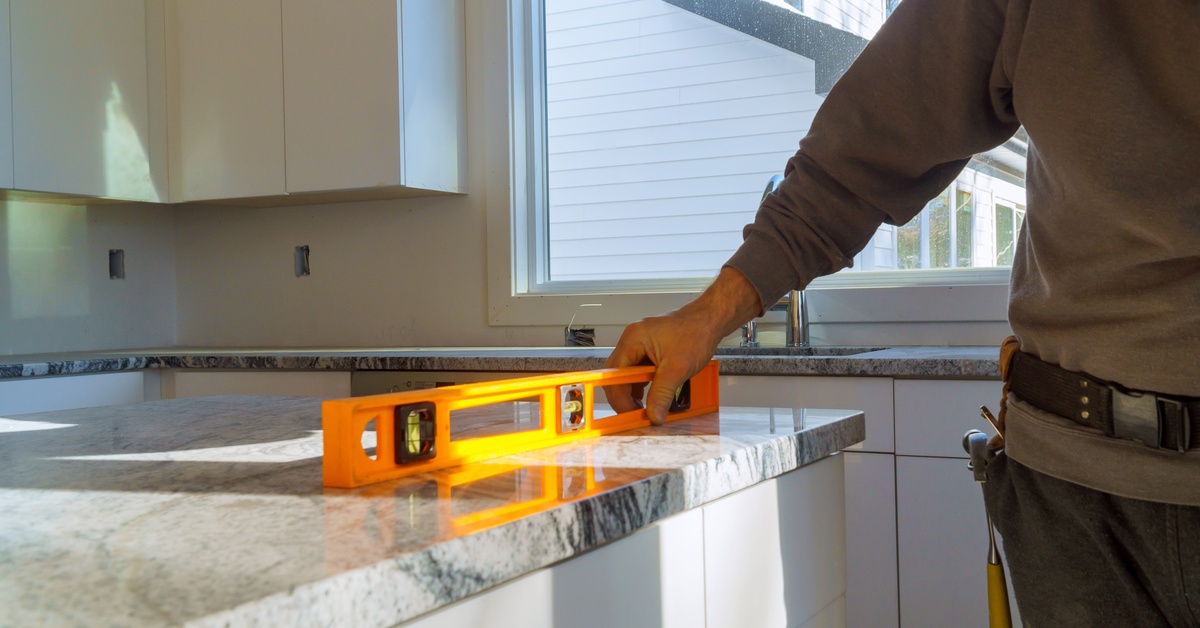 A close-up of a construction worker's hand as they use a leveler to see if the gray-stoned countertop is leveled.